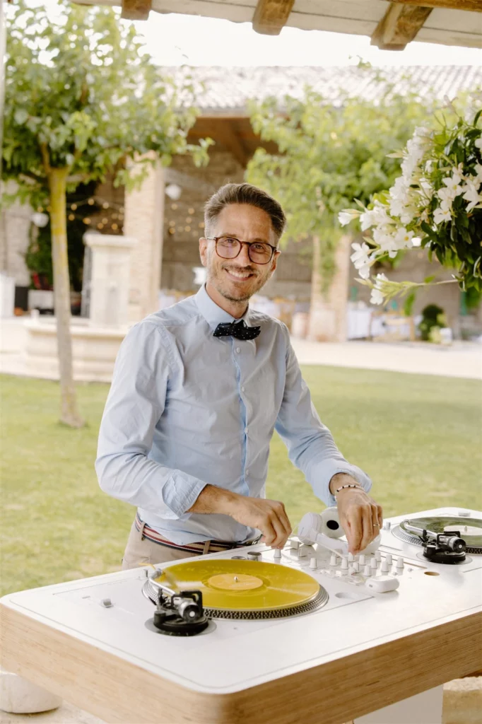 Benjamin de Nuit Blanche DJ souriant en plein mix sur les platines du bar vinyles lors d'un mariage au Domaine de Sarson